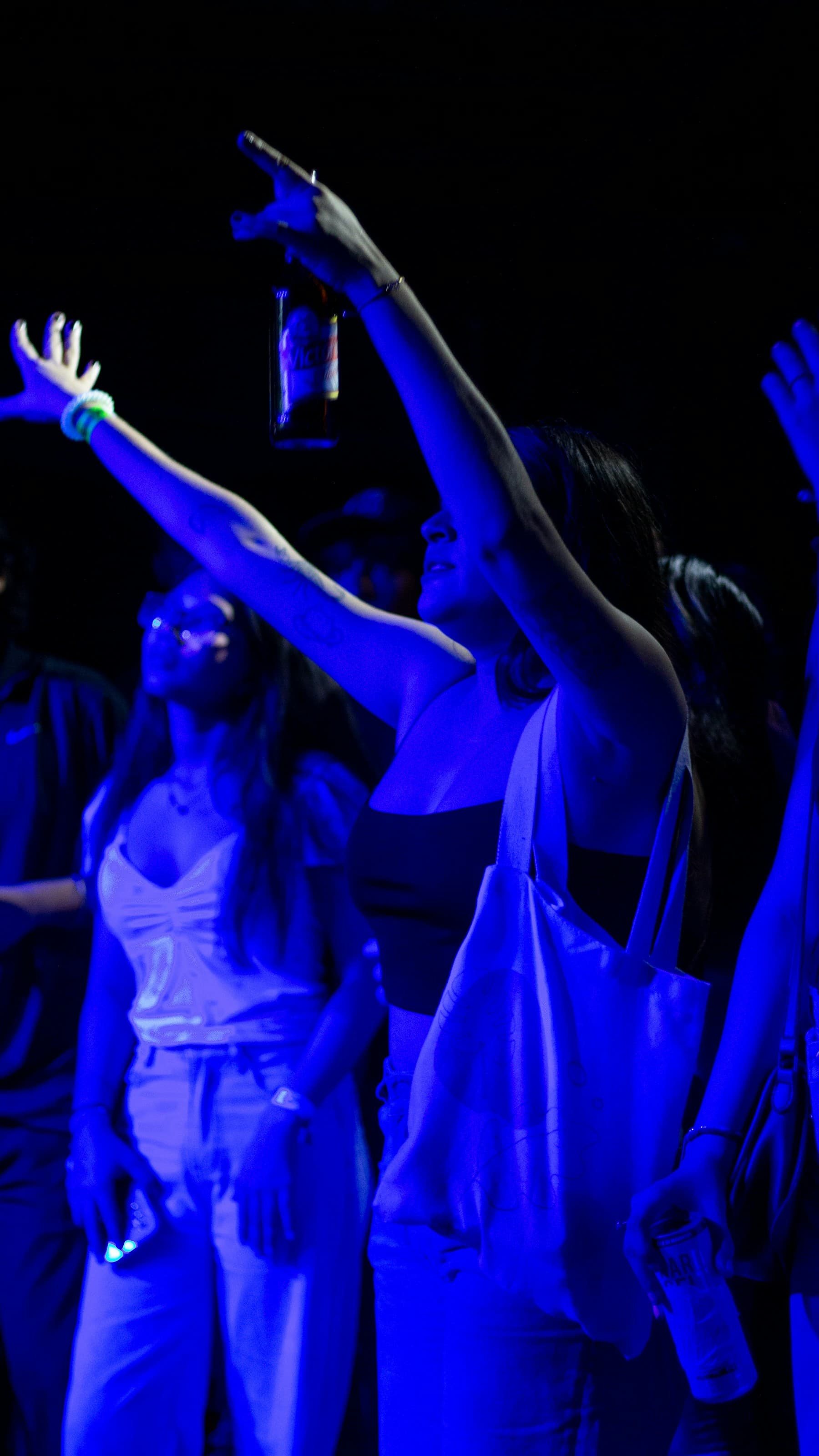 Bezoekers met opgeheven armen in intens blauw nachtlicht